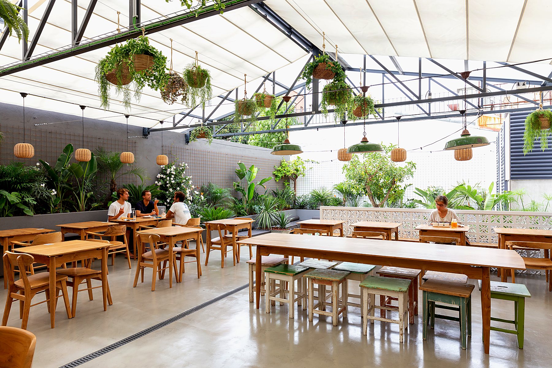 Jardim interior da MadPizza de Alvalade, com mesas de madeira, plantas suspensas e cobertura de vidro